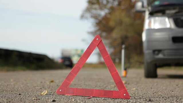 A warning triangle and a car stand on the side of the road.