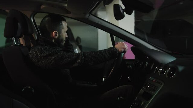Nervous driver talking on the phone at the parking lot and gesturing emotionally. Side view of a man sitting in the car and making a phone. Stressed guy talking in auto
