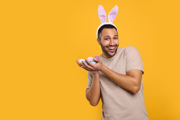 Happy African American man in bunny ears headband with Easter eggs on orange background, space for...
