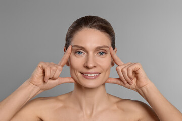 Woman massaging her face on grey background