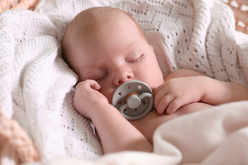 Cute newborn baby with pacifier sleeping on white blanket, closeup