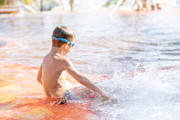A boy in snorkeling goggles sits in the pool and creates splashes