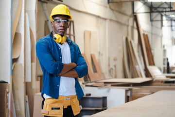 Male carpenter standing in carpentry workshop. A multiracial repairman at work in wood furniture building factory. Portrait of joiner man with protective gear worker standing in woodwork manufacturing