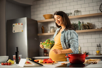 Young woman cutting vegetables in kitchen. Beautiful pregnant woman making salad