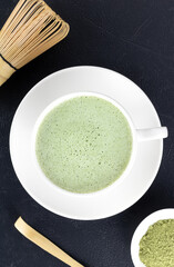 Traditional matcha green tea latte in white cup and bamboo whisk on black table. Top view.