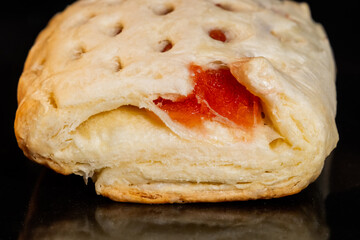 Front view: puff pastry bun with red strawberry jam baking and rising on tray in electric oven - close up, black background. Homemade bakery, food, cooking and pastry concept