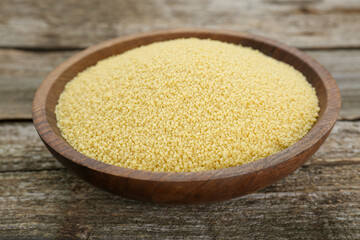 Bowl of raw couscous on wooden table, closeup