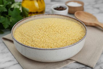 Bowl of raw couscous on white marble table, closeup