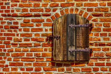 a small wooden window closed with wooden shutters in the middle of a brick wall.