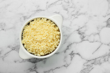 Bowl of tasty couscous on white marble table, top view. Space for text