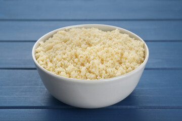 Bowl of tasty couscous on blue wooden table, closeup