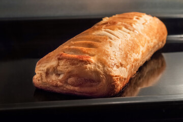One baked puff pastry bun with apple jam on tray in electric oven - close up view. Homemade bakery, food, cooking and pastry concept