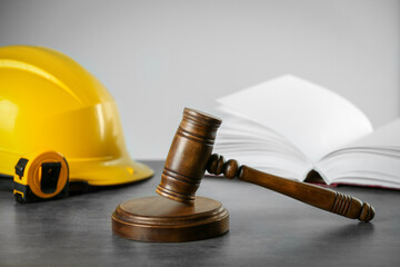 Construction and land law concepts. Judge gavel, open book, tape measure with protective helmet on grey table