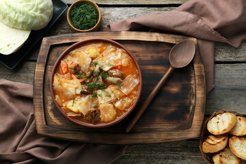 Tasty cabbage soup with meat, carrot and ingredients on wooden table, flat lay