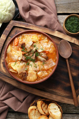 Tasty cabbage soup with meat, carrot and ingredients on wooden table, flat lay