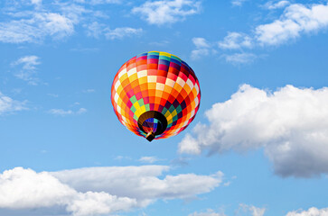 Colorful hot air balloon flying over blue sky with white clouds