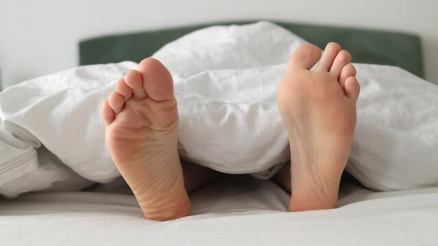 Woman's barefoot in close-up, funny shaking from side to side, lying on bed. Dry soles. Concept of vacation and rest.