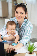 Fototapeta premium mom is using a laptop while holding her baby