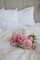 A beautiful bouquet of peonies and ranunculus flowers on the empty unmade bed with white sheets. A romantic surprize for st. Valentine's day. Close up, copy space, background, top view, natural light
