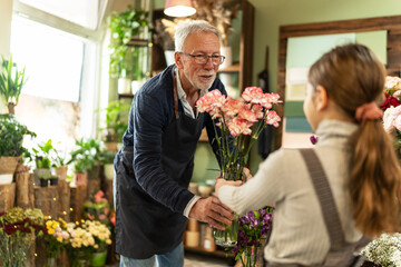 Senior florist working in his shop and teaching his granddaughter about plants and flowers.