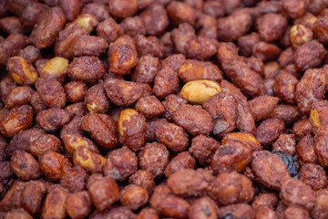 Heap of roasted caramelized sugared peanuts background at summer outdoor food market - close up. Cookery, dessert, gastronomy and street food concept
