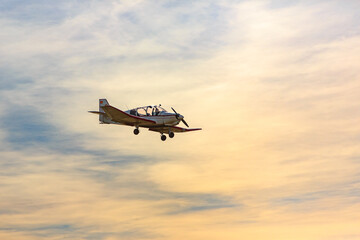 Single-engine airplane flies against the backdrop of sunset and the woman pilot waves her hand.