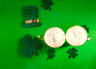 Two mugs of cold beer on green background with shamrock and hat, from above, st patrick's day