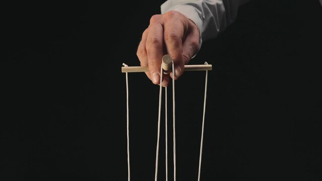 The puppeteer's hand controls the puppet with a wooden manipulator and strings. The marionettist controls and pulls the strings on a black isolated background. Close up.