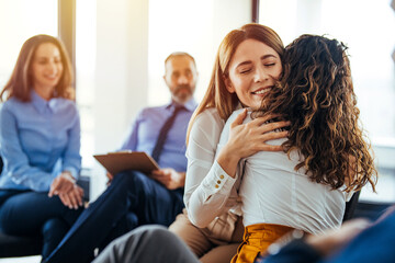 Portrait of female psychologist embracing young woman during therapy session in support group. Side view portrait of young woman embracing woman during therapy session in support group, copy space