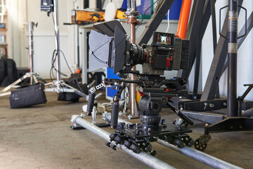 a professional movie camera stands on the set on a camera trolley with wheels on rails. various tripods and fixtures around