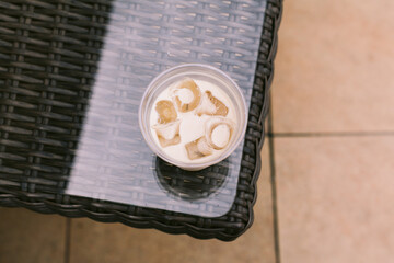 Cold coffee with milk and ice in plastic cup, top view. Summer drink to go standing on veranda table