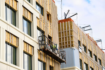 Robot builders who insulate walls of facade of multi-storey residential building with mineral insulation, while on construction cradle. Heat saving concept.