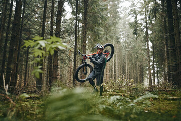 Rider carrying his mountain bike along a forest trail