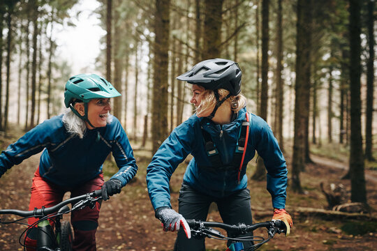 Smiling mother and daughter mountain biking in a forest
