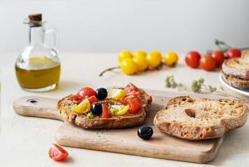 Friselle are typical Italian twice-baked bread, here topped with red and yellow tomatoes, olive oil, olives and oregano on cutting board