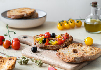 Friselle are typical Italian twice-baked bread, here topped with red and yellow tomatoes, olive oil, olives and oregano on cutting board