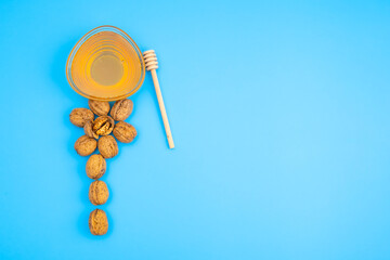 A bowl with honey and a flower from pecan walnuts on a blue background as a concept of healthy eating, dieting and fasting