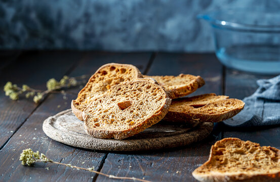 Friselle are typical Italian double-baked bread on wooden table with dark grey background, water in back stage for soaking Friselle before topping and eating