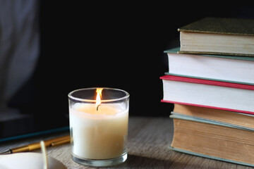 Pile of books, tablet, reading glasses, mobile phone, scented candle, pen and laptop on the table. Selective focus.