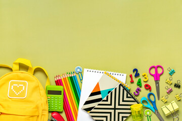 Back to school, education concept Yellow backpack with school supplies - notebook, pens, eraser rainbow, numbers isolated on green background Top view Copy space Flat lay composition Banner