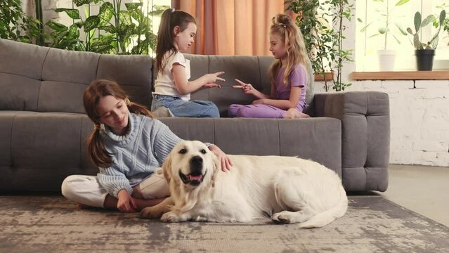Little girls, children playing on sofa, hugging cute dog od golden retriever in the living room on daytime. Relaxation. Concept of family, childhood, pets, care, friendship, emotions. leisure
