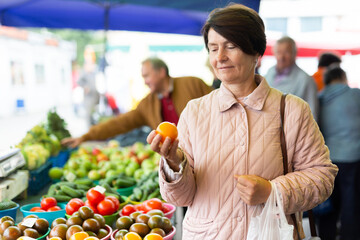 Obraz premium Aged woman customer buying vegetables in open-air market