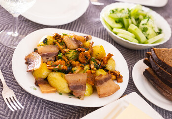 baked potatoes with chanterelles and bacon served with herbs and lightly salted cucumbers on table