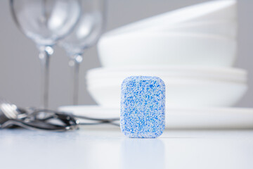 Dishwashing tablet and clean white dishes on white background
