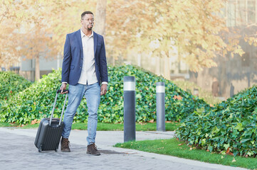Handsome young African businessman carrying a suitcase walking through the financial district. He...