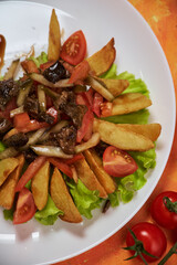 warm salad with meat and potato wedges, vegetables and herbs. on a bright colored background with vegetables