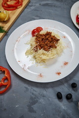 pasta with cheese, vegetables, meat on a white plate. with tomatoes and cheese around the edges on a gray background