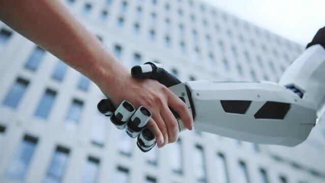 Horizontal footage of human and machine. Caucasian man shaking robot hand on blurred background of modern building outdoors. Agreement concept. Business automation. Handshake