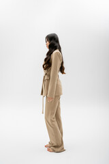 full length of barefoot asian model in fashionable suit standing on grey background.