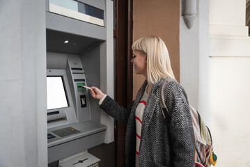 Young backpacker girl withdraws cash money from an ATM machine with her credit card to continue...